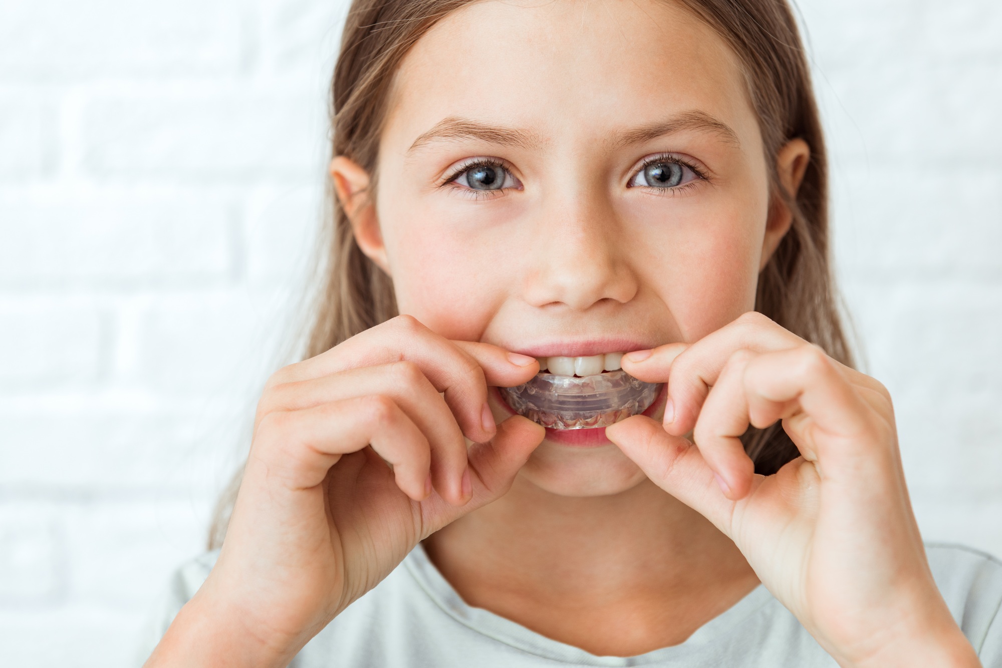 Attractive little girl stands on white background. Dental simulator for teeth alignment .