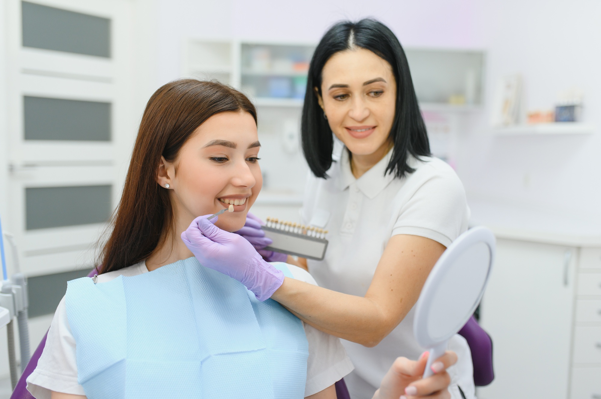 Dentist checking and selecting color of young woman's teeth