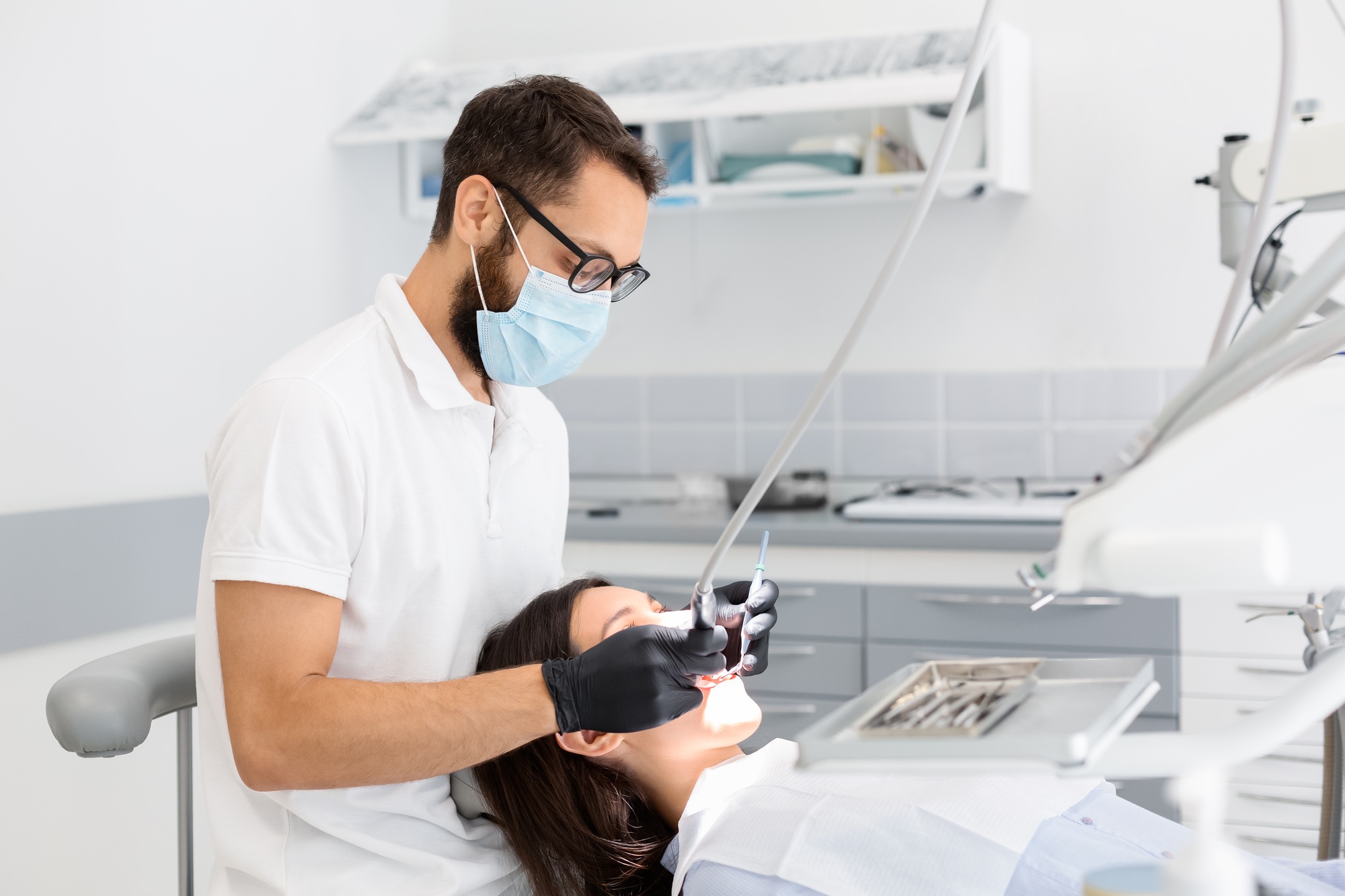 Dentist doctor in glasses filling teeth to female patient