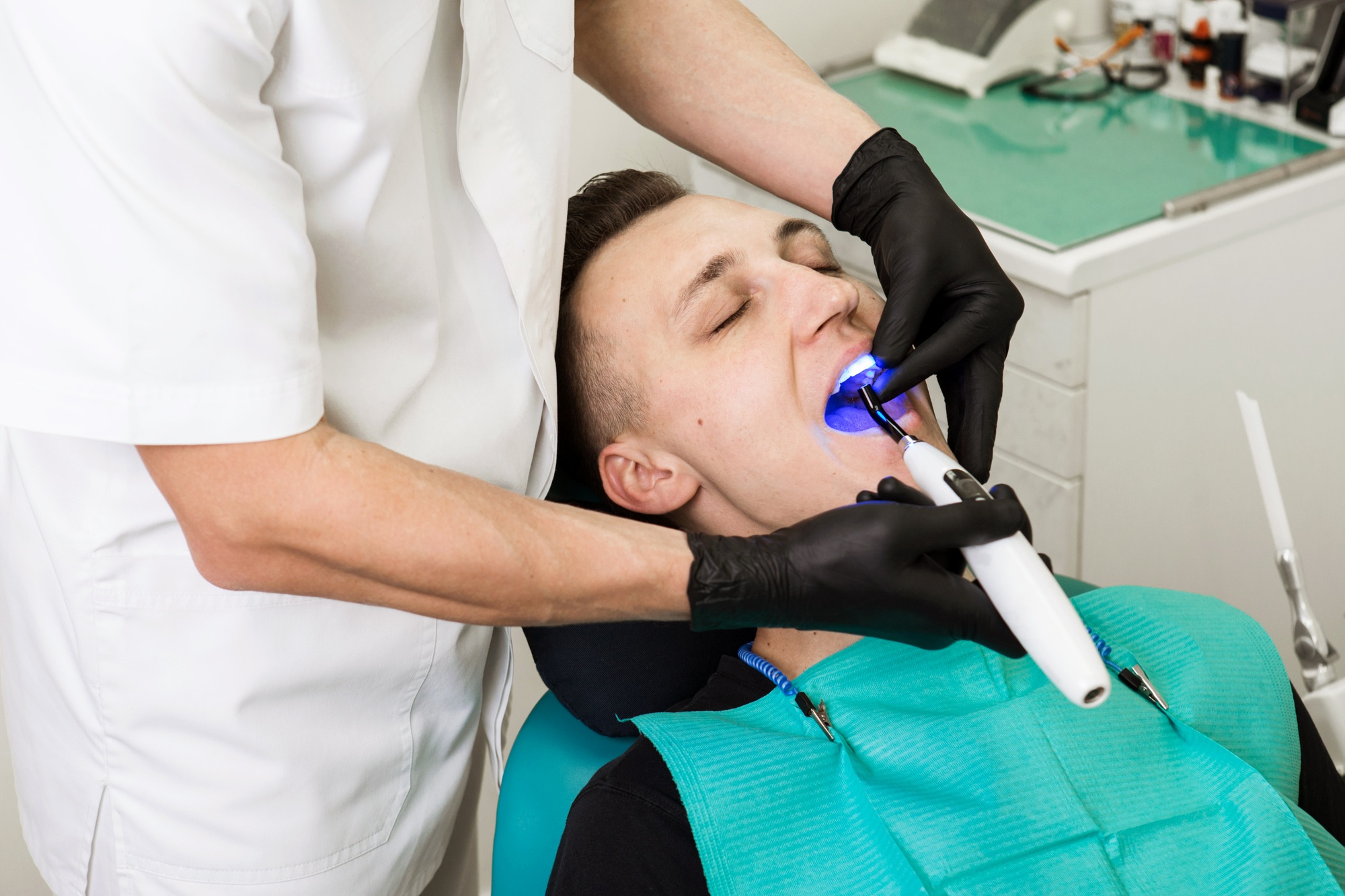 Dentist shine a bright blue Light in the male patient's mouth to harden composite filling. Dental