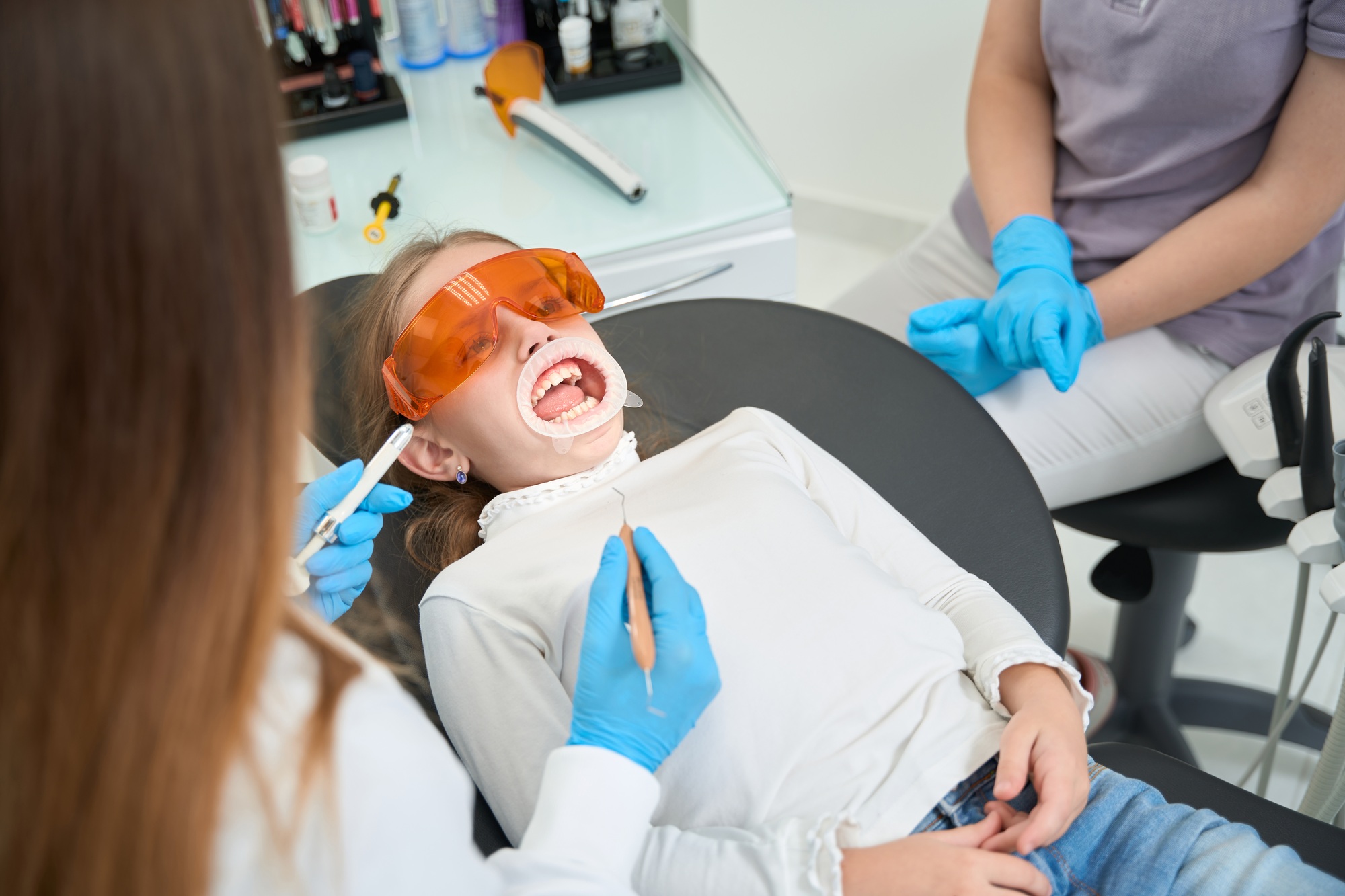 Pre-teen girl surrounded by dental staff before teeth examination