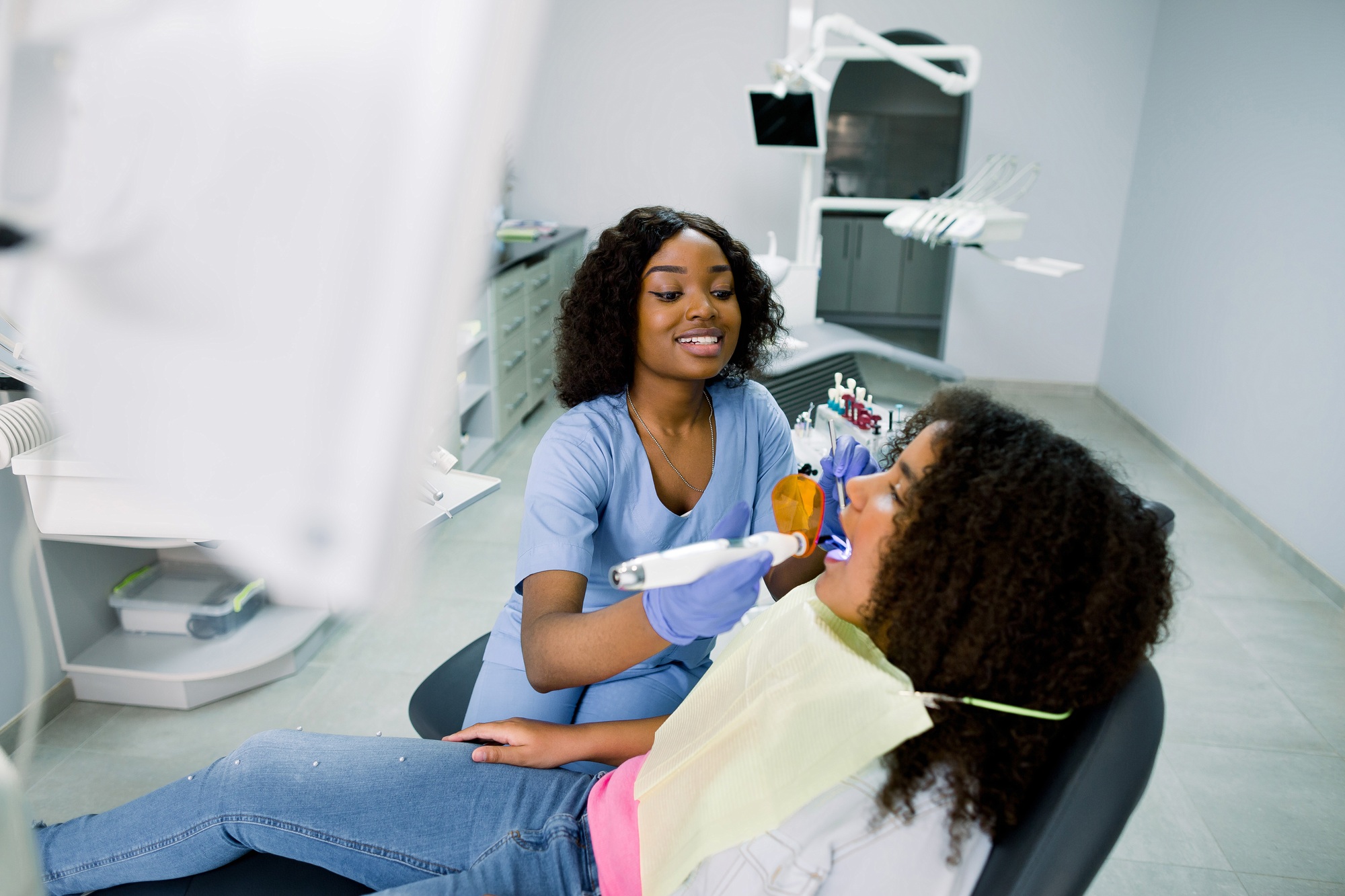 Smiling black woman dentist wearing blue uniform, providing tooth restoration
