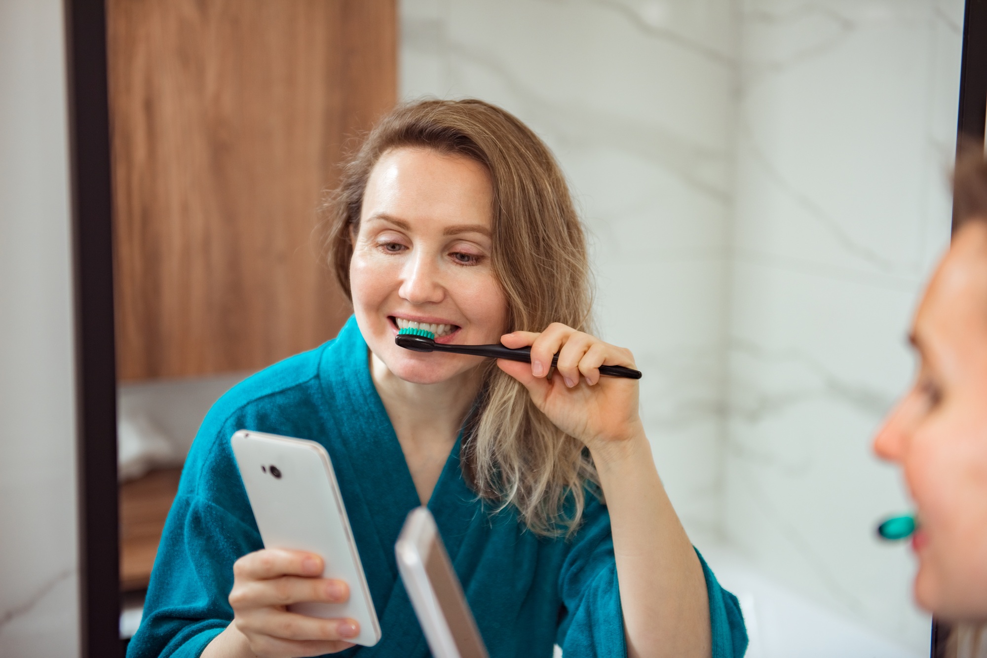 Social media affect. Young happy woman brushing teeth and looking at phone screen