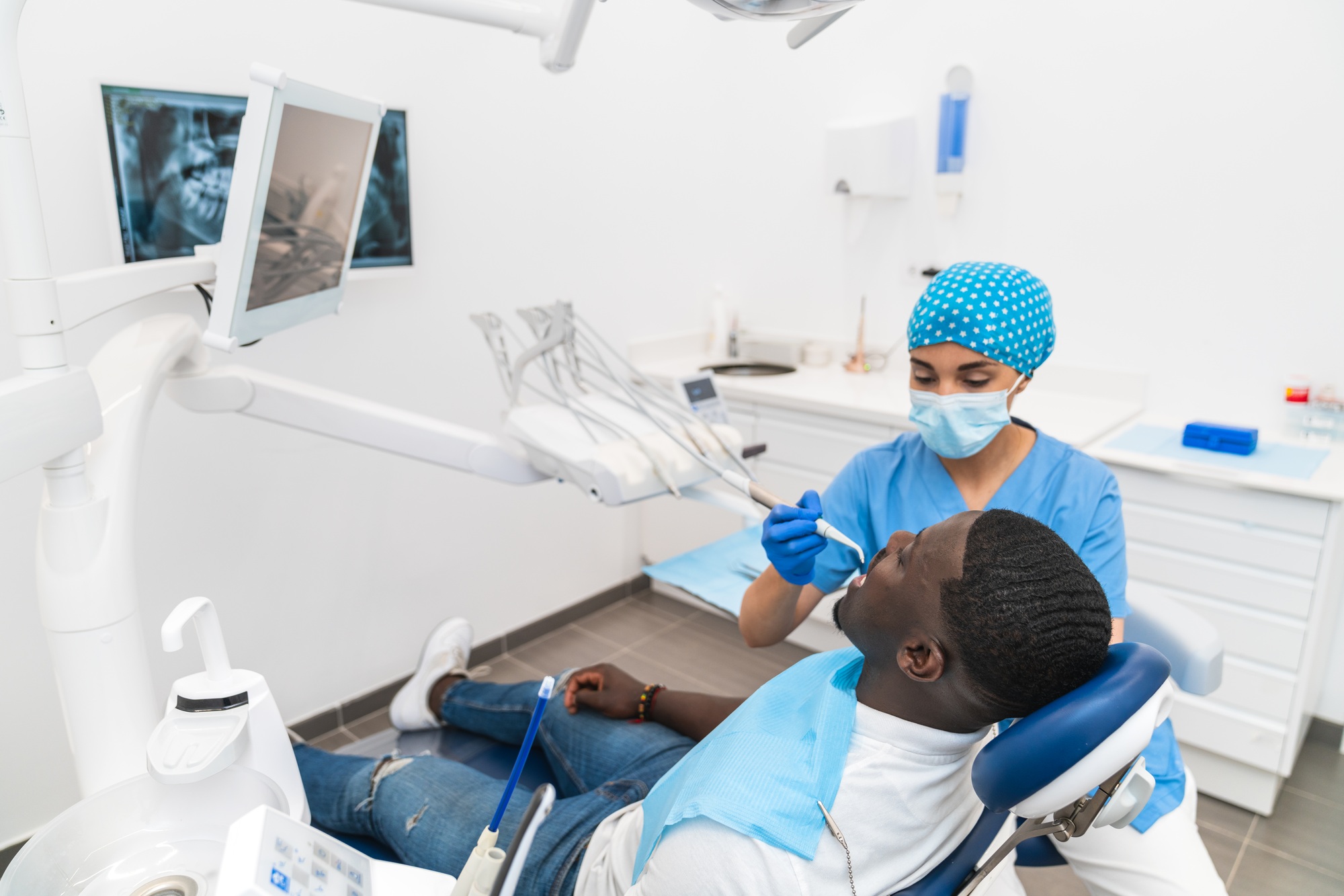 Dental hygienist performing a dental cleaning procedure on an African male patient in the clinic.