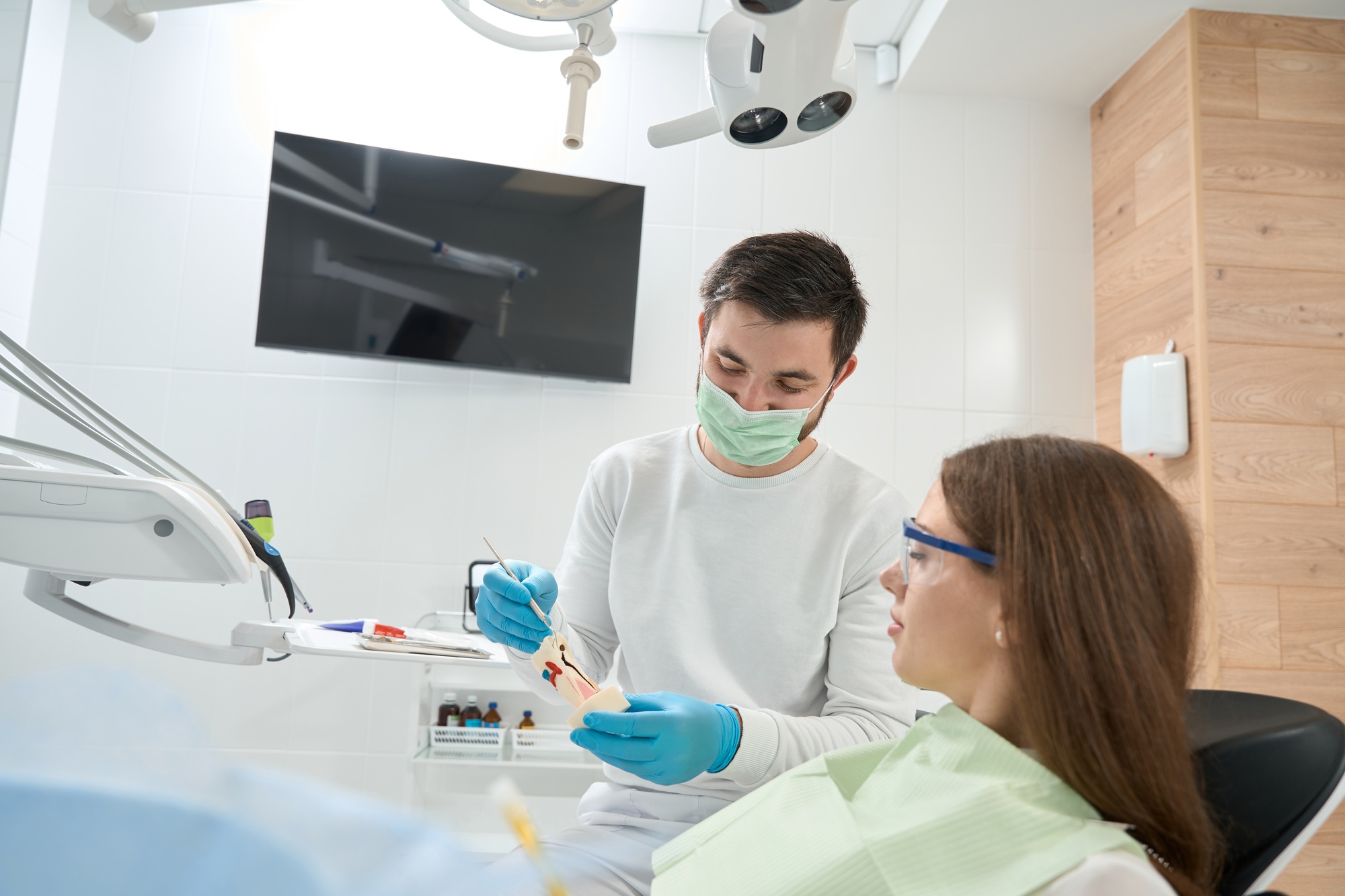 Dentist demonstrating carious tissue to female client seated in chair