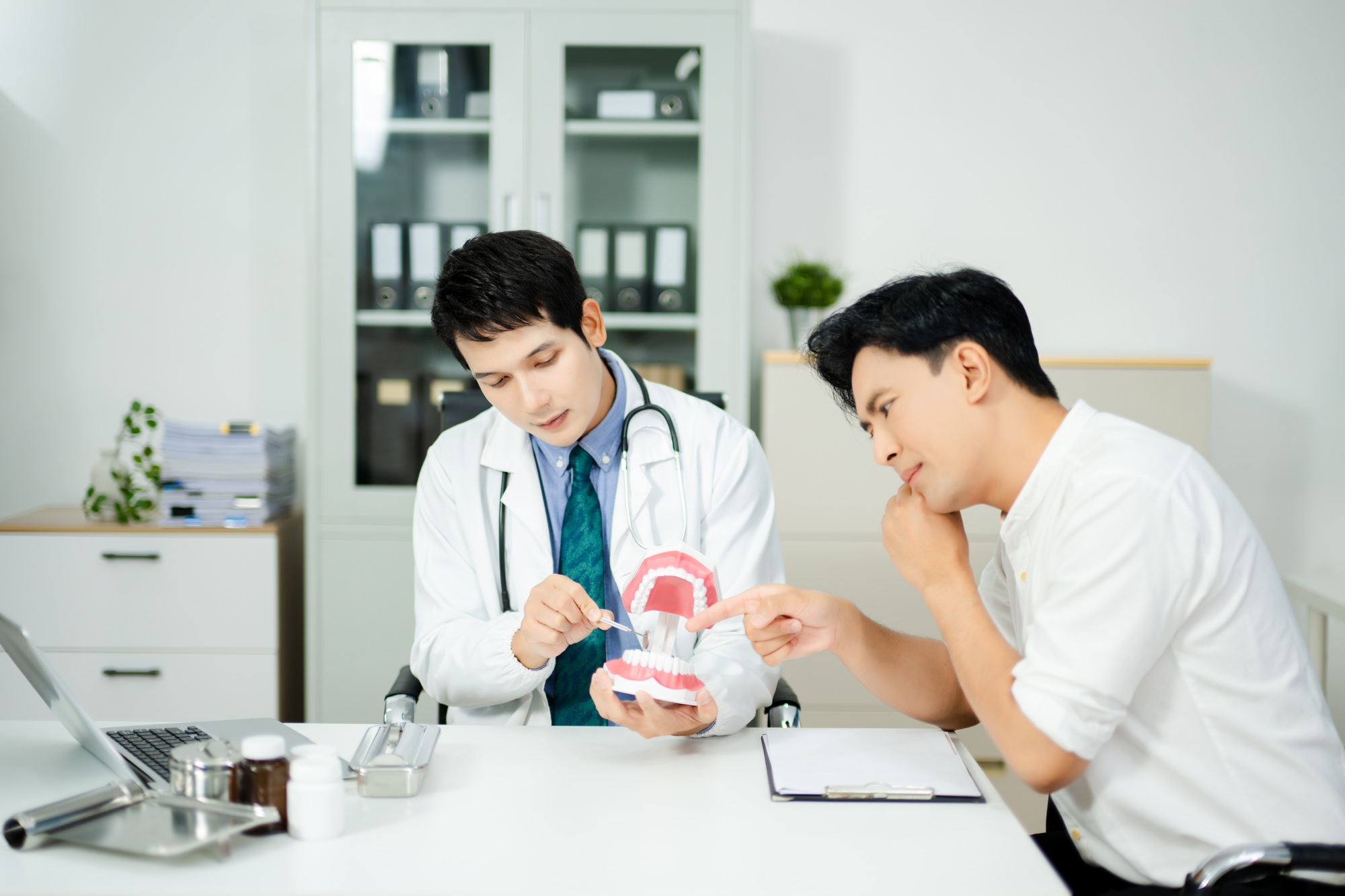Dentist explaining dental care to male patient using a tooth model. Health consultation,