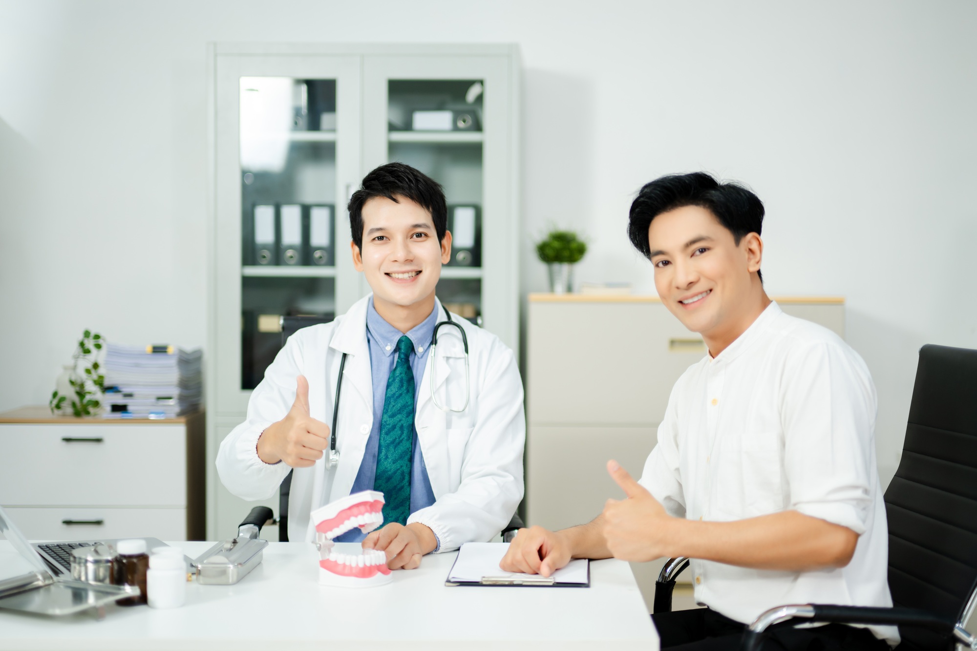 Dentist explaining dental care to male patient using a tooth model. Health consultation,