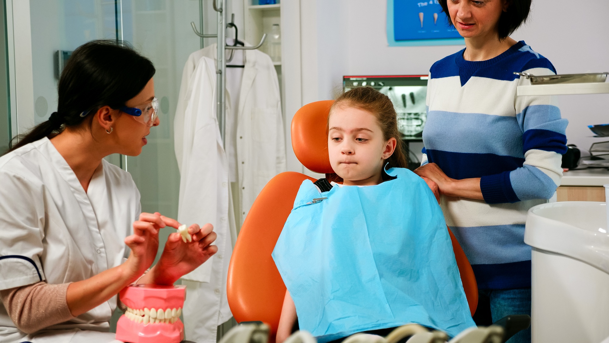 Dentist explaining to girl procedure of extraction using model of dental teeth
