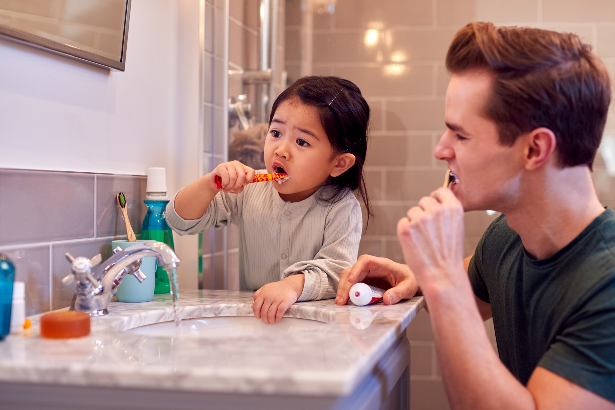 Family With Dad And Daughter Brushing Teeth In Bathroom At Home Together