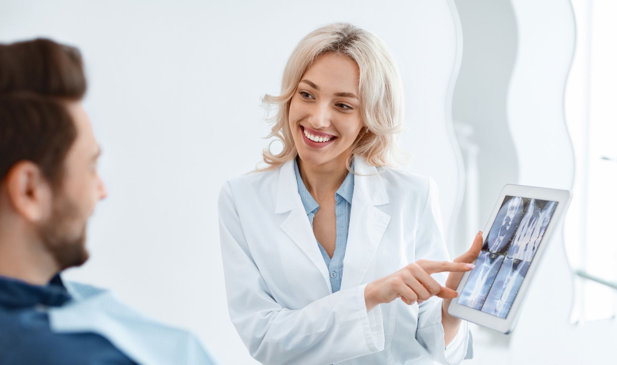 Female dentist showing male patient x-ray on digital tablet