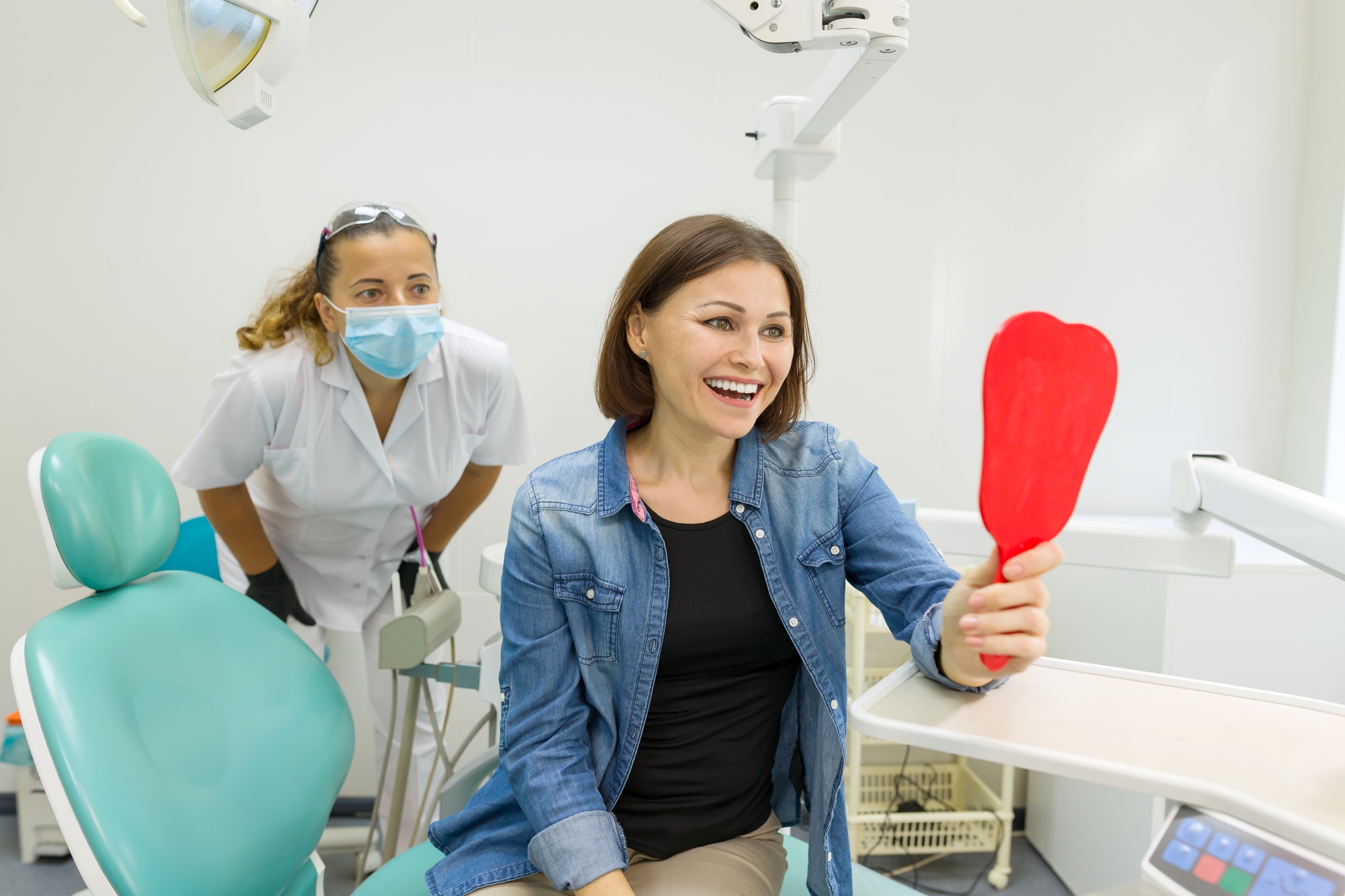 Happy woman patient looking in the mirror at the teeth, sitting in the dental chair