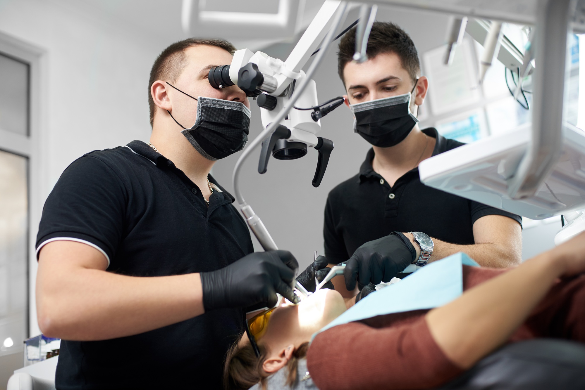 Male dentist in a black uniform fixing patient's teeth