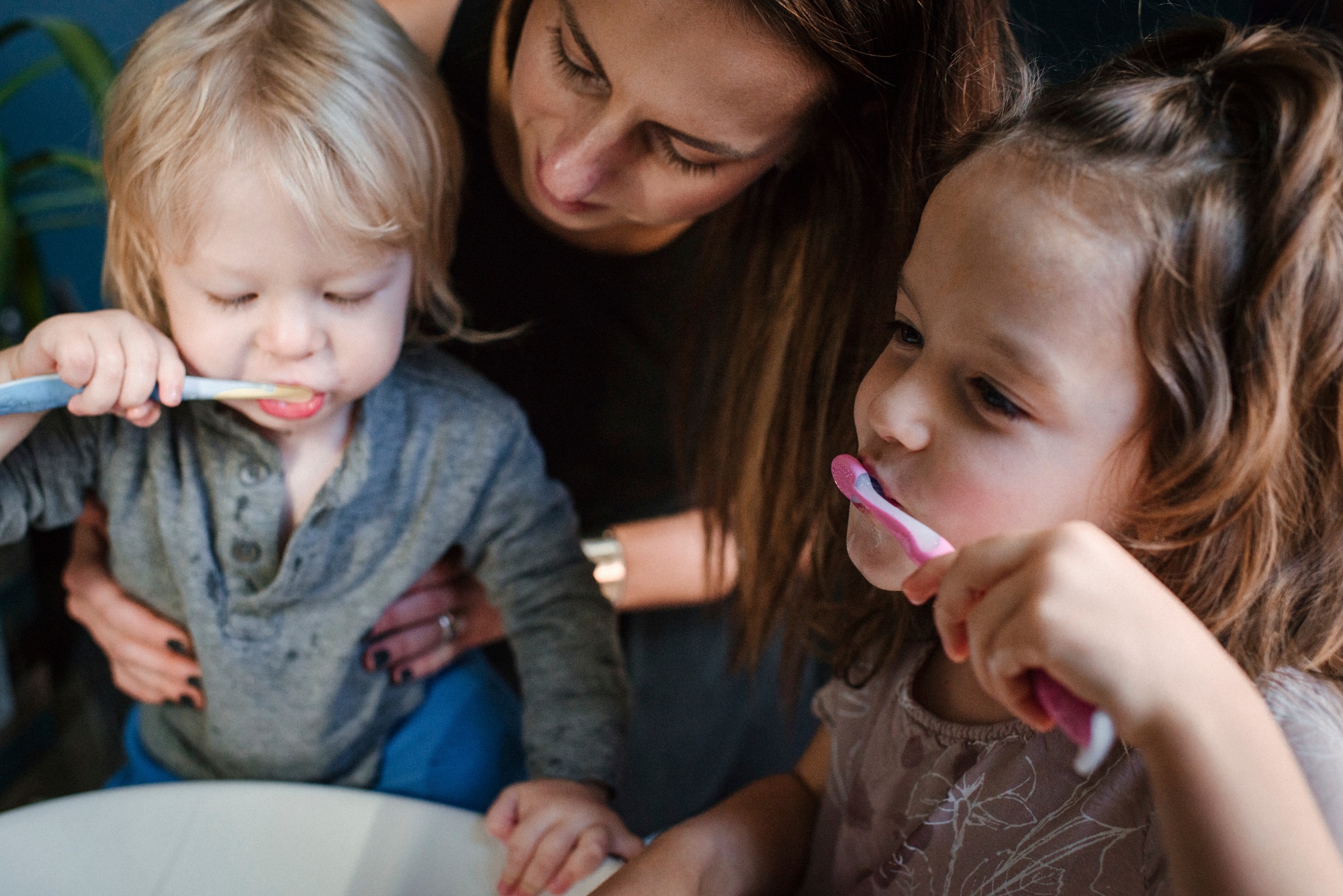 Mother helping children brush teeth