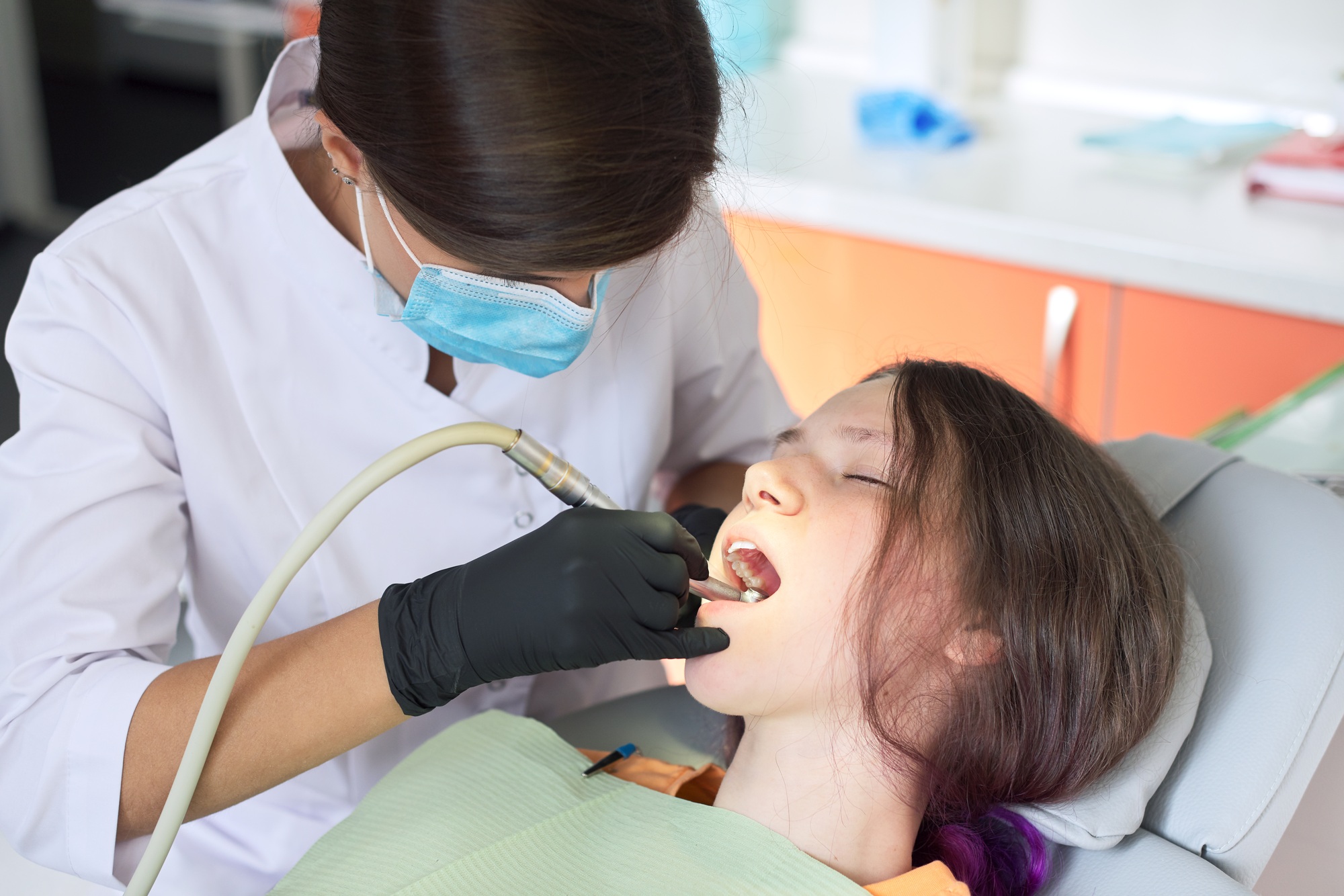 Woman dentist treating teeth to a patient sitting in dental chair using professional equipment