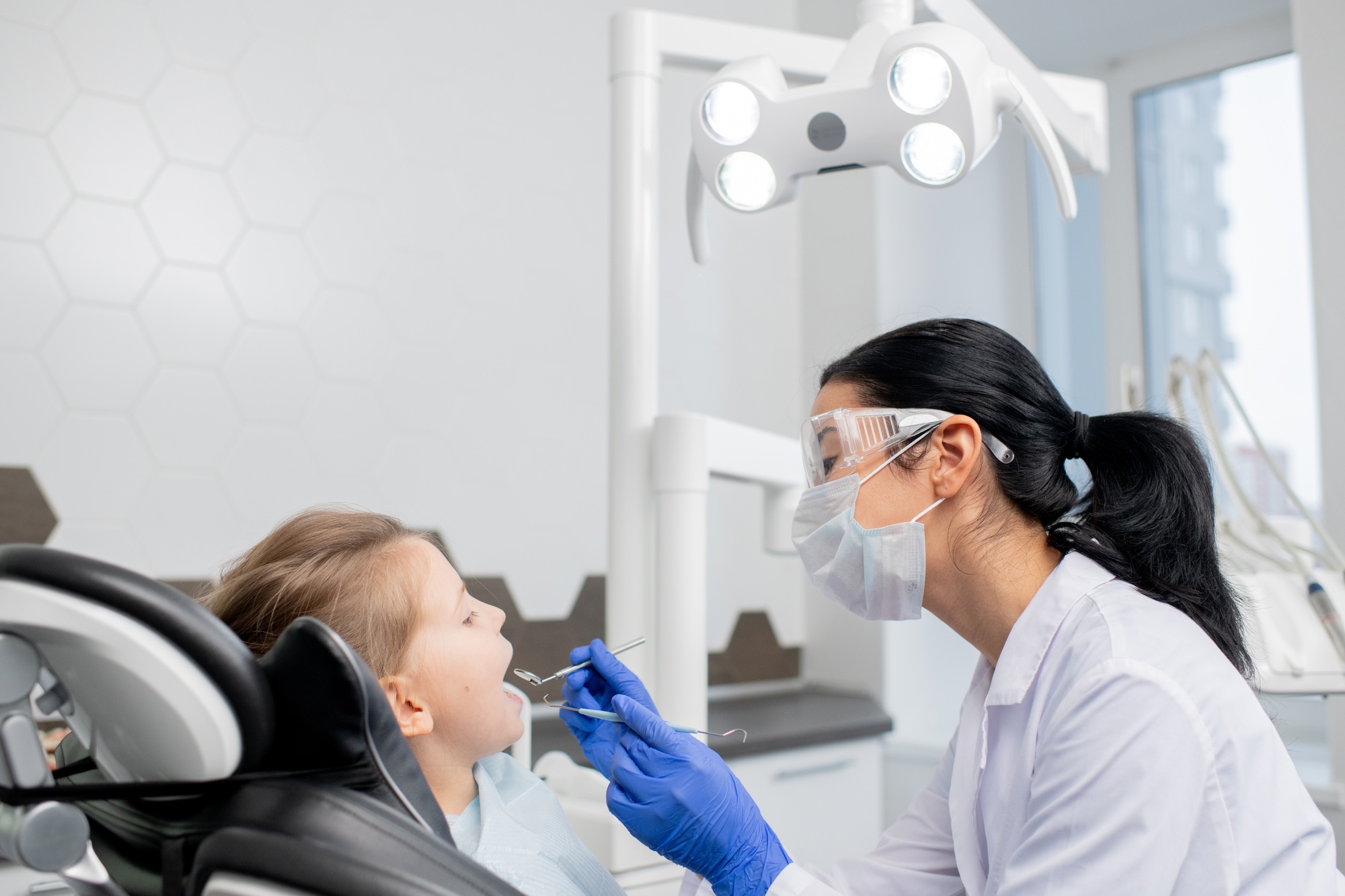 Young female dentist going to do oral checkup of oral cavity of little patient